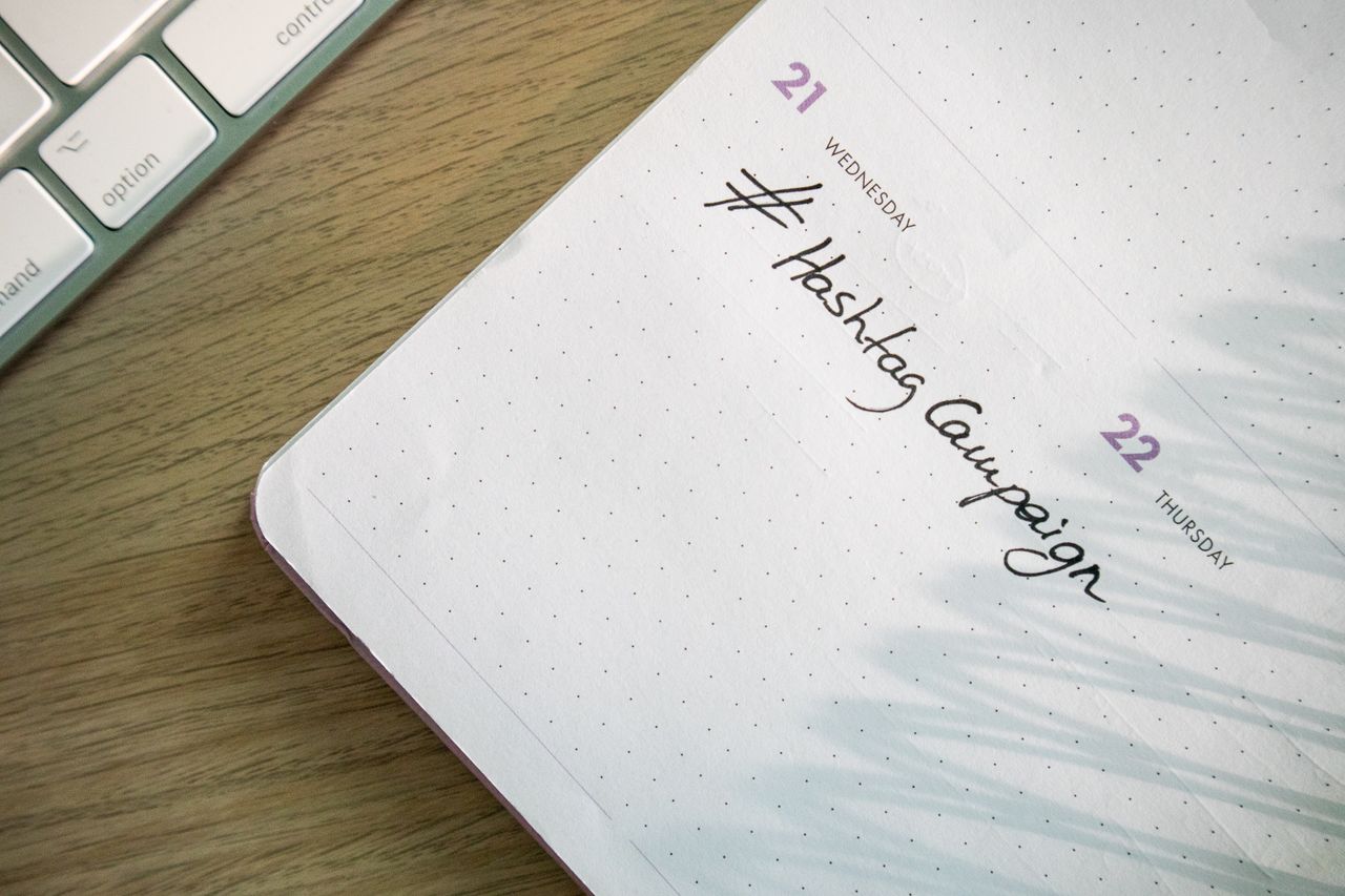 An open planner with “Hashtag Campaign” written by hand beside a keyboard. Great for social media and productivity themes.